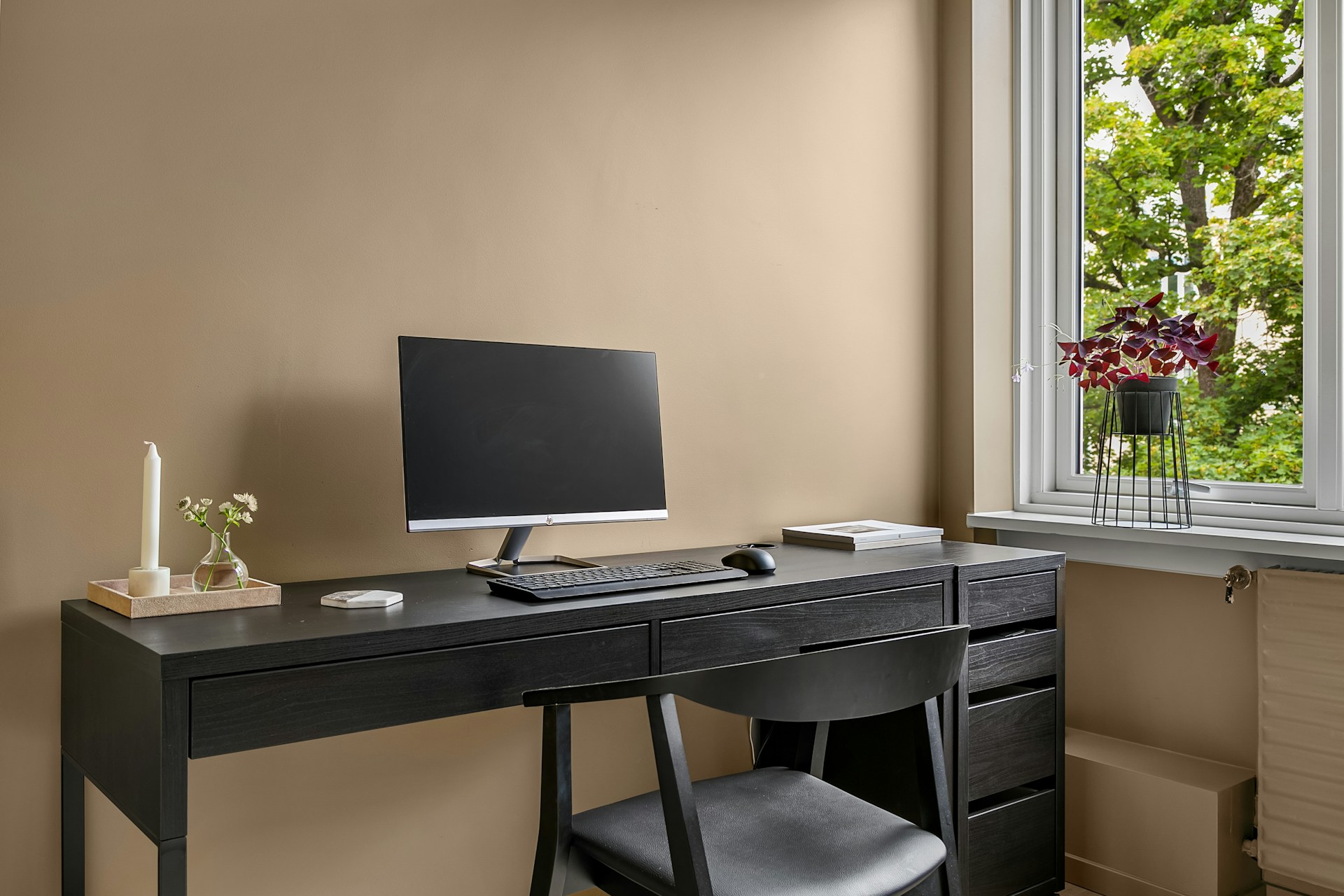 Skrivbord vid ett fönster med dator och anteckningsblock